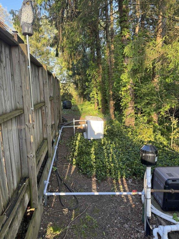 Completed installation of 28kW Generac standby generator with 200-amp automatic transfer switch at residential property. Mounted generator unit on concrete pad in backyard area adjacent to existing wooden privacy fence. Ran gas line from existing service point to generator location, with final length determined following zoning approval. Installed exterior electrical panel and transfer switch on brick wall near existing meter base, utilizing red conduit for line connections. Wired transfer switch to main electrical panel with appropriate gauge conductors and established proper grounding. Connected generator to transfer switch via conduit run along exterior wall. No disconnect installation was required per electrical specifications. Tested automatic transfer switch operation and verified generator startup sequence. System is fully operational and ready for automatic backup power during utility outages.