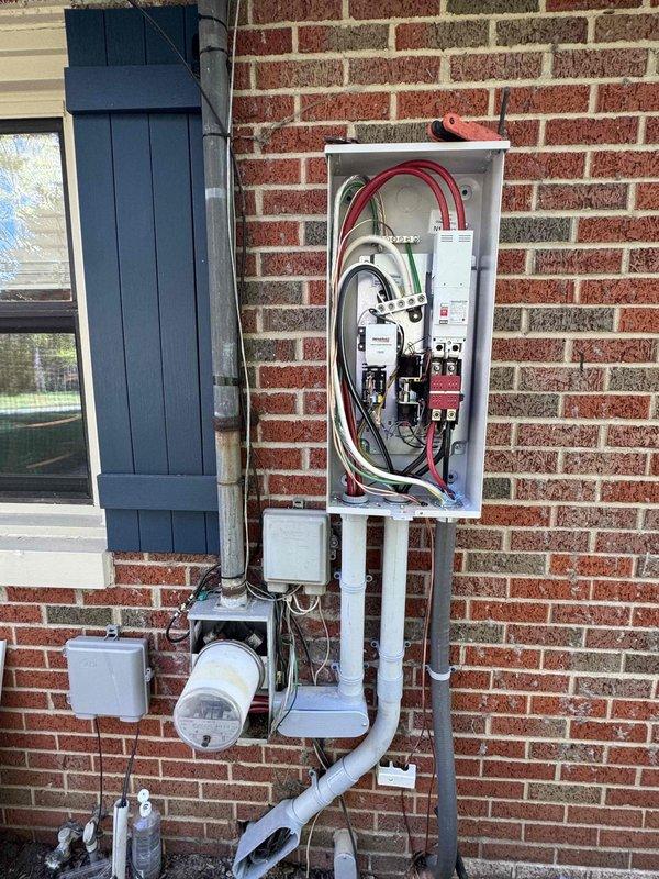 Completed installation of 28kW Generac standby generator with 200-amp automatic transfer switch at residential property. Mounted generator unit on concrete pad in backyard area adjacent to existing wooden privacy fence. Ran gas line from existing service point to generator location, with final length determined following zoning approval. Installed exterior electrical panel and transfer switch on brick wall near existing meter base, utilizing red conduit for line connections. Wired transfer switch to main electrical panel with appropriate gauge conductors and established proper grounding. Connected generator to transfer switch via conduit run along exterior wall. No disconnect installation was required per electrical specifications. Tested automatic transfer switch operation and verified generator startup sequence. System is fully operational and ready for automatic backup power during utility outages.