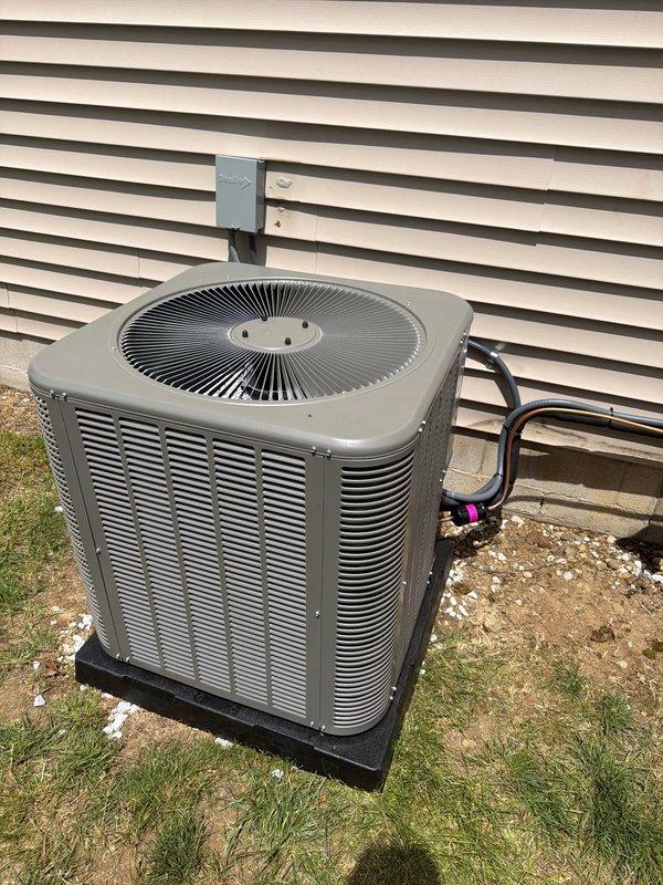 Completed full HVAC system installation including outdoor condensing unit and associated electrical components. Installed beige 80,000 BTU air conditioning unit on rubber isolation pad with proper clearances from building structure. Routed refrigerant lines through building penetration with appropriate sealing and secured lines to exterior wall. Mounted electrical disconnect box on building exterior per code requirements and installed FLNR 25 amp Littelfuse fuses in dual fuse holder assembly for proper overcurrent protection. Verified all electrical connections, tested system operation, and confirmed proper airflow through louvered intake panels and top-mounted fan assembly.