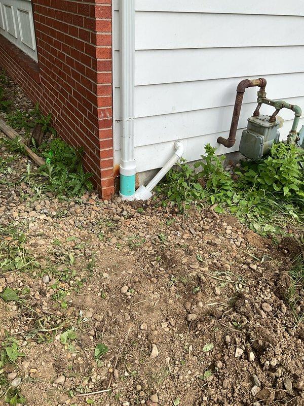 Excavated and replaced existing underground downspout drainage line on right side of residential property from rear roof leader to city connection point. Connected existing underground downspout from sunroom roof leader to new drainage system. Relocated sump pump discharge from underground to above-grade installation and integrated into downspout drainage system. Verified proper pitch throughout entire drainage line to ensure adequate water flow and drainage performance. Backfilled excavated areas and mounded soil to accommodate natural settling. All PVC drainage piping installed to code specifications with appropriate fittings and connections at roof leader tie-in points and city connection terminus.