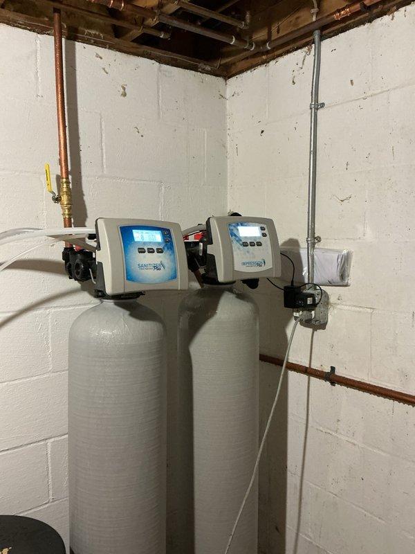 Completed recurring salt delivery service for dual-tank water softener system. Delivered and replenished water softener salt pellets from warehouse inventory to basement utility area, filling the designated salt storage container adjacent to the water treatment equipment. System confirmed operational with both softener tanks displaying proper digital readouts and all plumbing connections secure with no visible leaks or issues.