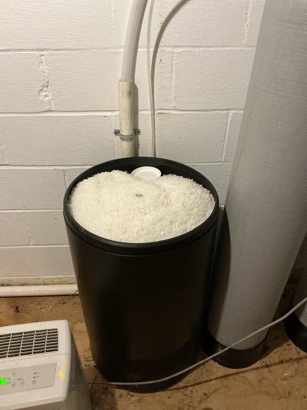 Completed recurring salt delivery service for dual-tank water softener system. Delivered and replenished water softener salt pellets from warehouse inventory to basement utility area, filling the designated salt storage container adjacent to the water treatment equipment. System confirmed operational with both softener tanks displaying proper digital readouts and all plumbing connections secure with no visible leaks or issues.