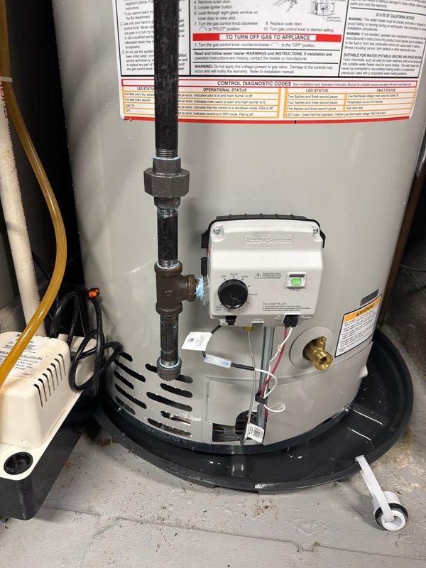 Completed installation of Bradford White tanked water heater in residential utility room. Unit was positioned on black drain pan with proper clearances maintained per manufacturer specifications. Connected hot and cold water supply lines using copper piping with brass fittings at top of tank. Installed pressure relief valve with discharge piping. Configured gas supply connection and venting system using appropriate metallic ductwork. Mounted Honeywell control system with temperature dial and indicator light to tank exterior. Established all electrical connections including power supply and grounding. Verified proper operation of all safety features and control mechanisms. Unit tested and confirmed operational with no leaks detected at any connection points.
