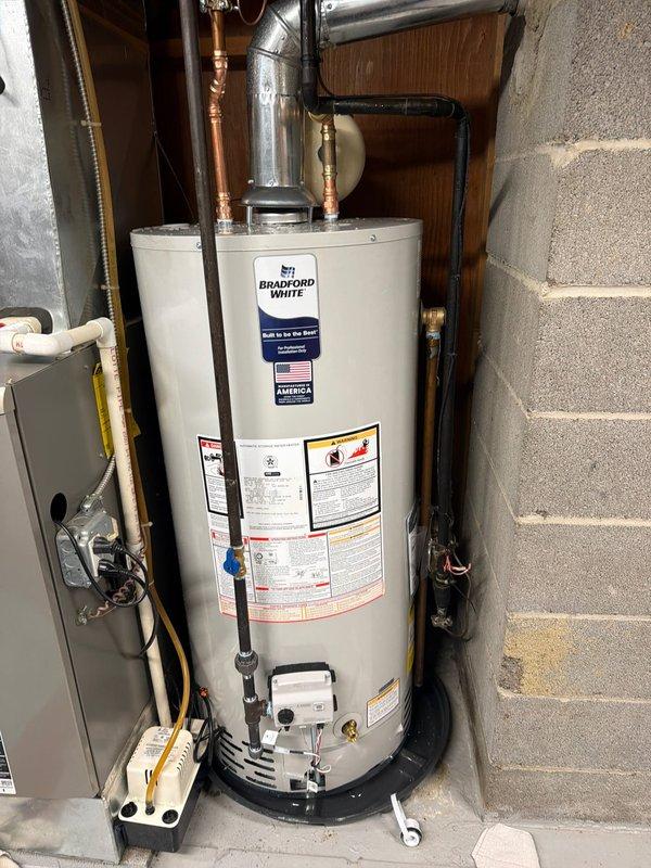 Completed installation of Bradford White tanked water heater in residential utility room. Unit was positioned on black drain pan with proper clearances maintained per manufacturer specifications. Connected hot and cold water supply lines using copper piping with brass fittings at top of tank. Installed pressure relief valve with discharge piping. Configured gas supply connection and venting system using appropriate metallic ductwork. Mounted Honeywell control system with temperature dial and indicator light to tank exterior. Established all electrical connections including power supply and grounding. Verified proper operation of all safety features and control mechanisms. Unit tested and confirmed operational with no leaks detected at any connection points.