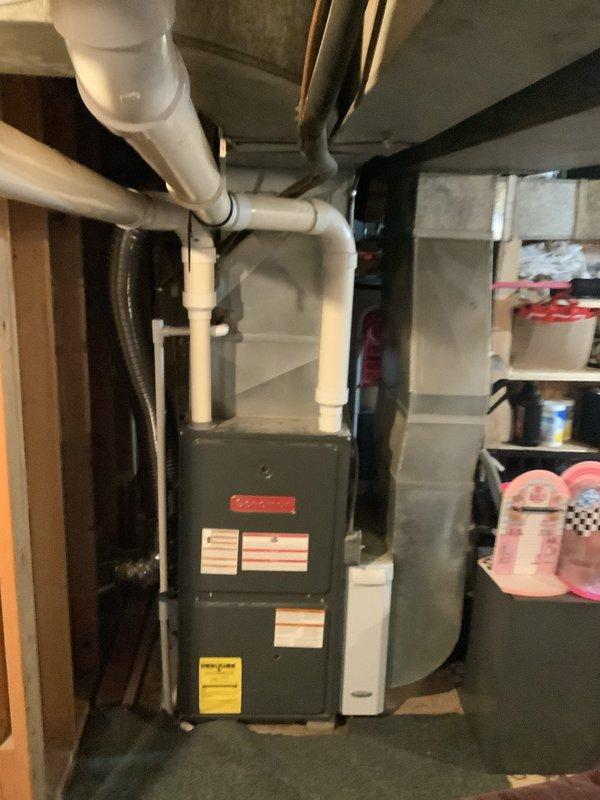 Completed installation of new air conditioning system including outdoor condenser unit and indoor evaporator coil. The outdoor condenser was positioned in the side yard with proper clearance from the building, refrigerant lines were run up the exterior wall, and electrical connections were completed. Inside the basement, the new evaporator coil was integrated with the existing furnace system, with PVC condensate drain lines properly routed and secured to prevent water damage.