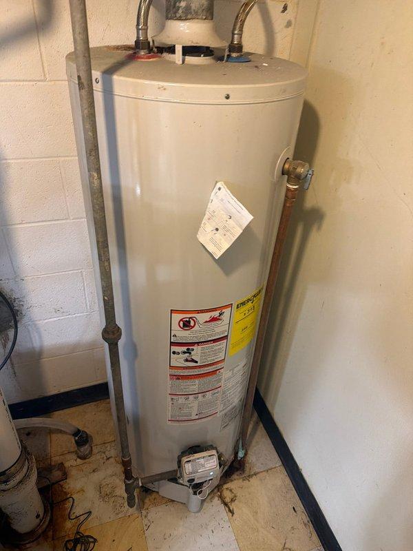 Responded to service call for leaking water heater over 10 years old. Upon inspection, confirmed active leak from aging tank-style natural gas water heater installed in basement utility room. Unit showed signs of deterioration consistent with age, including corrosion at connection points and compromised tank integrity. Due to age of equipment and extent of leak, recommended full replacement rather than repair. Documented existing installation with photos showing flexible supply lines, gas connections, venting configuration, and overall condition of mechanical space for replacement planning purposes.