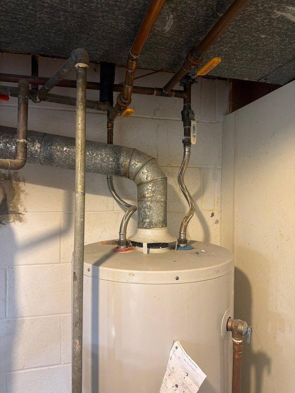 Responded to service call for leaking water heater over 10 years old. Upon inspection, confirmed active leak from aging tank-style natural gas water heater installed in basement utility room. Unit showed signs of deterioration consistent with age, including corrosion at connection points and compromised tank integrity. Due to age of equipment and extent of leak, recommended full replacement rather than repair. Documented existing installation with photos showing flexible supply lines, gas connections, venting configuration, and overall condition of mechanical space for replacement planning purposes.
