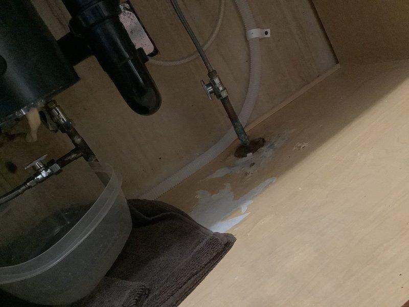 # Kitchen Sink Plumbing Leak Repair

Responded to service call for leaking kitchen sink piping near the dishwasher valve connection. Upon arrival, conducted diagnostic inspection of the under-sink plumbing system and identified active water leak at the dishwasher supply valve assembly. 

Water damage was evident on the cabinet floor substrate, with visible staining and moisture accumulation indicating ongoing leak condition. Inspected all supply lines, drain connections, and valve assemblies in the affected area. The metal valve assembly showed signs of corrosion and deterioration, which was determined to be the source of the leak.

Performed necessary repairs to the dishwasher valve connection, addressing the leak at the point of failure. Tested all connections under pressure to verify proper seal and confirm no additional leaks were present. Inspected adjacent plumbing components including flexible supply lines and mounting hardware to ensure system integrity.

Documented conditions 