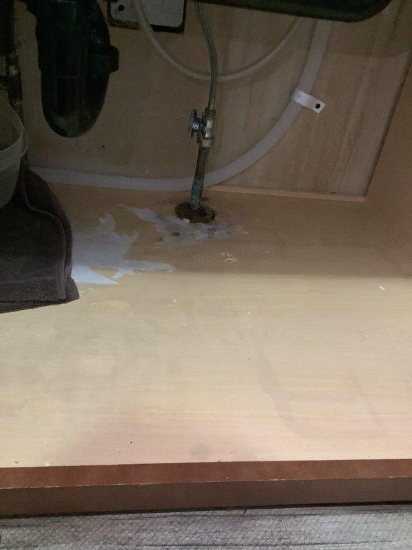 # Kitchen Sink Plumbing Leak Repair

Responded to service call for leaking kitchen sink piping near the dishwasher valve connection. Upon arrival, conducted diagnostic inspection of the under-sink plumbing system and identified active water leak at the dishwasher supply valve assembly. 

Water damage was evident on the cabinet floor substrate, with visible staining and moisture accumulation indicating ongoing leak condition. Inspected all supply lines, drain connections, and valve assemblies in the affected area. The metal valve assembly showed signs of corrosion and deterioration, which was determined to be the source of the leak.

Performed necessary repairs to the dishwasher valve connection, addressing the leak at the point of failure. Tested all connections under pressure to verify proper seal and confirm no additional leaks were present. Inspected adjacent plumbing components including flexible supply lines and mounting hardware to ensure system integrity.

Documented conditions 