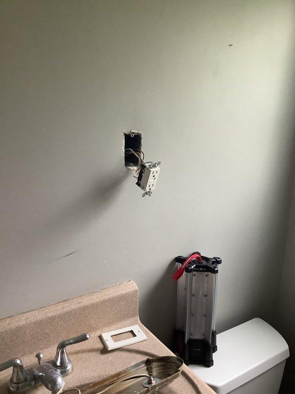 Installed new electrical outlet in bathroom wall to provide power for light fixture. Accessed existing electrical circuit through ceiling, ran appropriate wiring to outlet location, and installed junction box with proper connections. Patched and secured all ceiling and wall openings per code requirements.