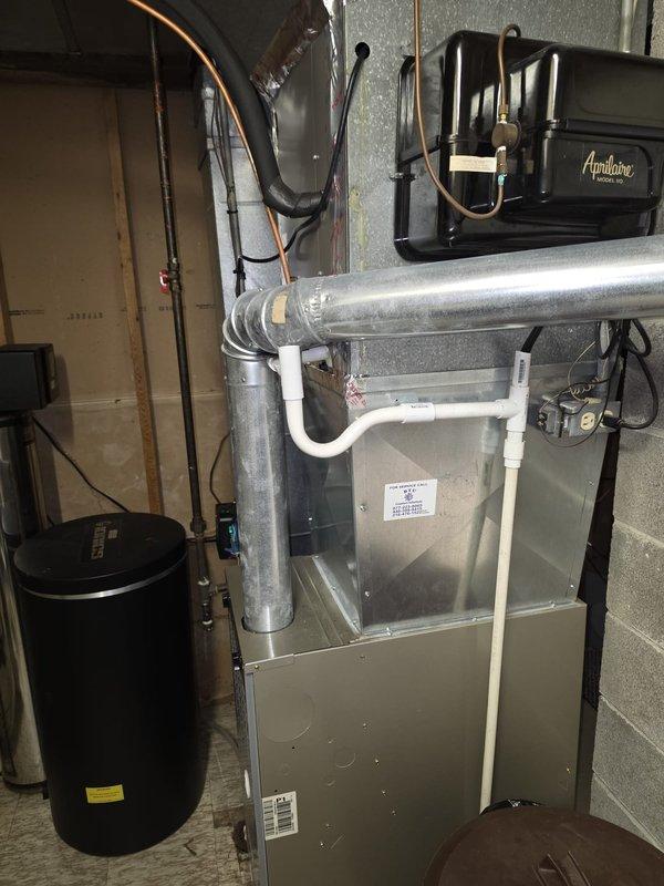# HVAC Install - A/C & Coil

Successfully completed installation of new air conditioning system including outdoor condensing unit and indoor evaporator coil. Installed gray cylindrical condenser unit on exterior concrete pad with proper clearances from structure. Mounted electrical disconnect box on siding with conduit run to unit. Inside mechanical room, integrated new evaporator coil with existing furnace/air handler system. Connected refrigerant lines between indoor and outdoor components using copper tubing with proper insulation. Installed condensate drainage system utilizing white PVC piping routed appropriately from coil. Verified all electrical connections meet code requirements. System tested for proper operation including refrigerant pressures, airflow, and temperature differential. Unit cycling correctly with all safety controls functioning as designed.