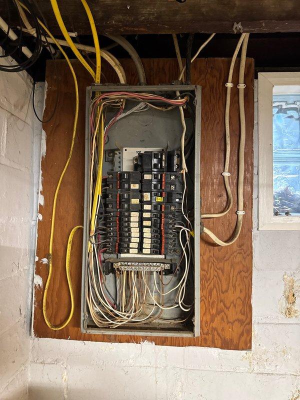 Completed 100-amp electrical service upgrade in basement utility area. Replaced aged and corroded electrical panel box showing extensive rust and deterioration with new panel installation mounted on wooden backing board. Installed new circuit breaker configuration with proper wire routing through ceiling joists, including color-coded branch circuits. Coordinated power disconnection with utility company prior to panel replacement to ensure safe working conditions during upgrade.