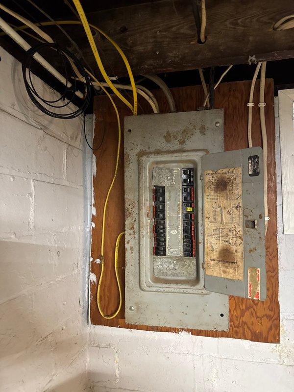 Completed 100-amp electrical service upgrade in basement utility area. Replaced aged and corroded electrical panel box showing extensive rust and deterioration with new panel installation mounted on wooden backing board. Installed new circuit breaker configuration with proper wire routing through ceiling joists, including color-coded branch circuits. Coordinated power disconnection with utility company prior to panel replacement to ensure safe working conditions during upgrade.