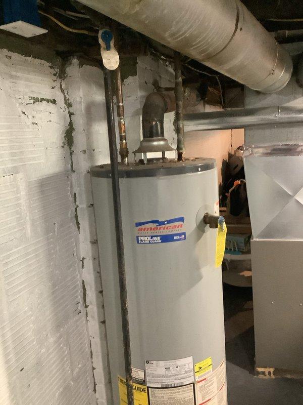 Responded to service call for leaking water heater. Upon inspection, found an American-brand tanked water heater showing visible signs of water leakage at the base with floor staining present. Unit is estimated to be over seven years old based on customer information. Evaluated overall condition of the water heater, including connections, pressure relief valve, and piping configuration. Documented current state with photographs showing the water heater installation, surrounding utility area, and evidence of moisture issues. Advised customer of findings and provided recommendation for water heater replacement due to age and active leak. Customer requested to be placed on cancellation wait list for expedited installation scheduling.
