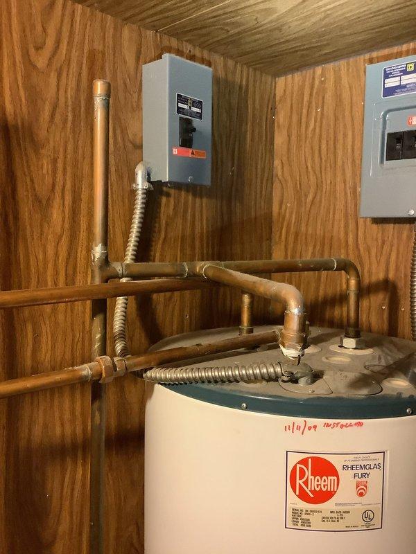 Responded to service call for 17-year-old Rheem water heater experiencing operational failure and unusual noises. Upon inspection, determined unit had reached end of serviceable life and required full replacement. Successfully removed old water heater and installed new Rheem residential tanked water heater unit, reconnecting all copper supply lines, brass fittings, and flexible connector hoses to existing plumbing infrastructure. Verified proper connections to overhead piping system, tested all valves for functionality, and ensured secure installation against wood-paneled utility room wall. System tested and restored to full operational status.