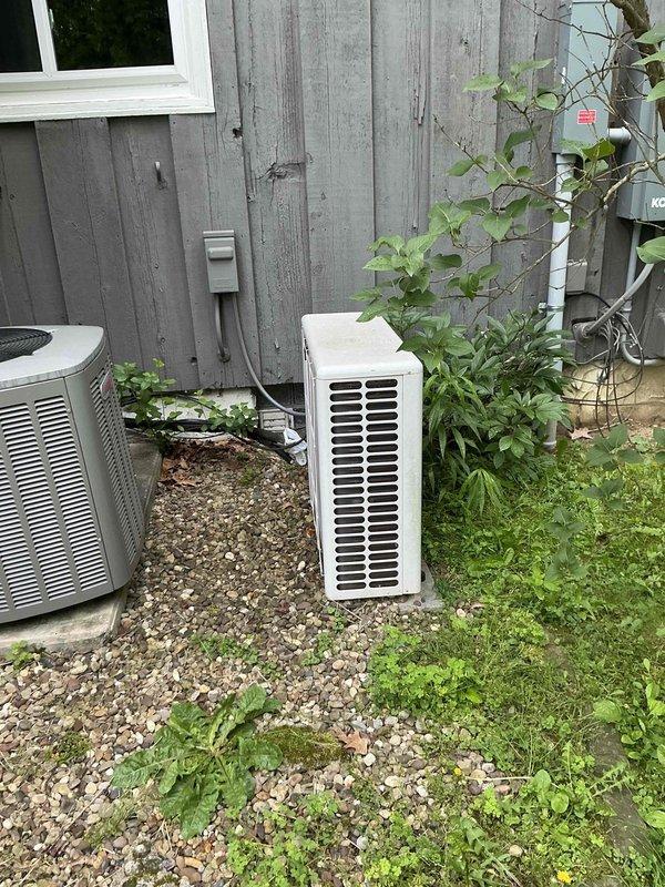 Provided estimate for Mitsubishi mini split system replacement to upgrade existing outdoor unit with different style configuration. Assessed current installation location with two condensing units on gravel pad adjacent to building with weathered siding, noted electrical disconnect box and conduit routing, and documented site conditions for proper equipment sizing and placement recommendations.