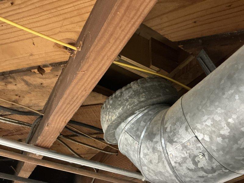 Conducted on-site assessment of 22-year-old residential air conditioning system for replacement estimate. Evaluated existing outdoor condenser unit with cylindrical design and horizontal fin configuration positioned on concrete pad against building exterior, noting age-related wear and system inefficiency. Inspected attic-mounted ductwork system, documenting metal duct routing through ceiling joists and assessing overall HVAC infrastructure condition to provide comprehensive replacement recommendations.