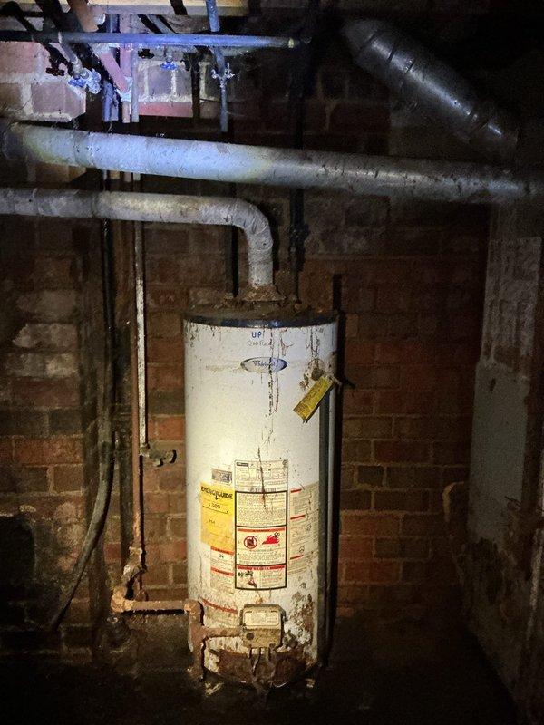 Provided quote for replacement of existing tanked water heater in 80-year-old residential property. Assessed current water heater installation located in basement utility area, noting aged unit with visible corrosion and wear on exterior tank surface. Evaluated existing plumbing configuration including copper supply lines, vent piping, and gas connections. Documented under-sink cabinet plumbing infrastructure and main water heater installation for replacement planning purposes.