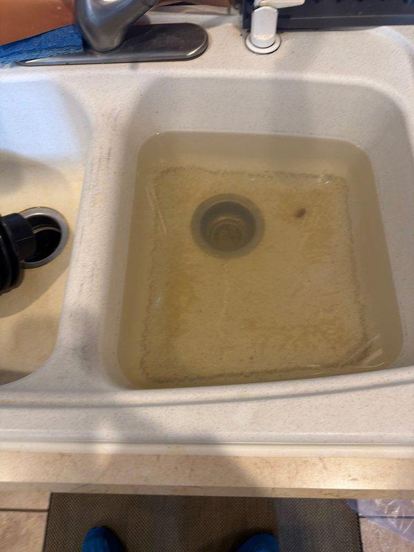 Responded to kitchen drain clog in double-basin sink where homeowner's previous attempts at clearing the blockage were unsuccessful. Upon arrival, found standing water with discolored, murky appearance in the right basin, indicating significant drainage obstruction. Assessed the plumbing system and determined the blockage location within the drain line. Utilized appropriate drain cleaning equipment and techniques to remove the clog, restoring proper water flow and drainage function to both basins. Tested the system to verify complete clearance and proper operation of the drain assembly. Documented conditions with photographs showing before and after states of the drainage issue.