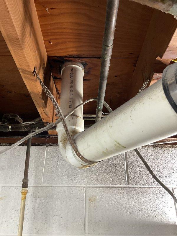 Responded to a toilet repair request in a 50-year-old home where the homeowner reported issues requiring a new wax ring and seal. Upon arrival, inspected the toilet installation and surrounding plumbing infrastructure, including overhead drain piping and floor drain connections. Documented existing conditions showing aged plumbing components with visible corrosion, staining, and mineral deposits on metal fixtures, indicating long-term water exposure and potential seal deterioration that would affect toilet performance and stability.