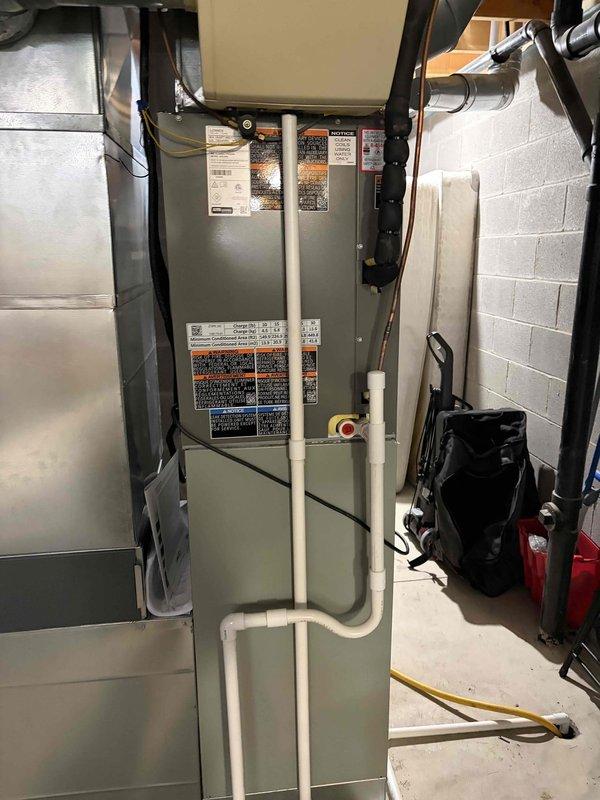 Completed full HVAC system installation including outdoor condensing unit and indoor air handler with evaporator coil. Installed new condensing unit on protective base pad with proper refrigerant line connections using insulated copper linesets—gray insulation on liquid line and black foam on suction line. Mounted air handler unit in basement utility area against block wall, established proper condensate drainage using white PVC piping with appropriate fittings routed to floor drain. Connected all refrigerant lines to both indoor and outdoor units using brass service valves, completed electrical connections, and verified all manufacturer specifications and warning labels are properly affixed to equipment. System installed per code requirements and manufacturer guidelines.