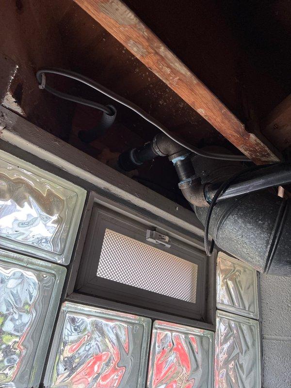 Installed new 480V AC circuit wiring with exterior conduit routing along building facade, securing dual parallel runs of rigid metal conduit with appropriate mounting hardware and weatherproof junction boxes. Completed interior basement wiring connections, routing conductors through floor joists and integrating with existing electrical infrastructure while maintaining proper clearances around glass block window installation and ventilation components.