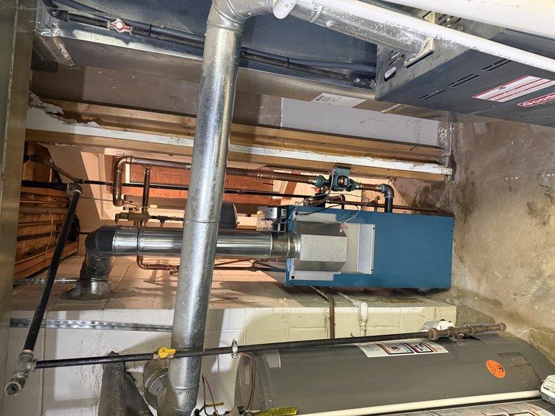 Successfully completed hot water boiler installation in basement mechanical room. Installed new blue residential boiler unit with accompanying gray expansion tank, configured with comprehensive copper piping manifold system featuring multiple zone distribution lines. System includes properly installed supply and return lines, zone valves, and all necessary connections for hydronic heating operation. Integrated new boiler with existing ductwork and HVAC infrastructure, ensuring proper venting and clearances per manufacturer specifications. All copper piping professionally soldered and secured, expansion tank properly mounted and pressurized, and system tested for leaks and proper operation. Installation meets current mechanical codes and manufacturer requirements for residential hydronic heating systems.