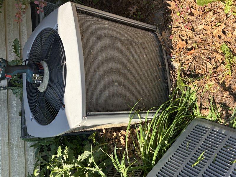 Performed comprehensive air conditioner tune-up on outdoor condensing unit. Conducted electrical diagnostics using digital multimeter to verify proper voltage and amperage readings, with measurements indicating system operating within normal parameters at approximately 50.5 volts during testing. Inspected condenser unit exterior condition, noting accumulated debris and weathering on mesh grill covering that required attention for optimal airflow and system efficiency.
