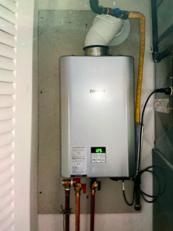Replaced existing Rinnai RL75 tankless water heater with new Rinnai 180 unit in utility area. Installation included mounting unit on concrete board backing, connecting copper water inlet and outlet lines with shut-off valves, installing yellow CSST gas line with safety shut-off valve, and routing white PVC venting through wall. Unit tested and operational with digital display functioning properly, all connections verified leak-free, and system staged with navigation kit per manufacturer specifications.