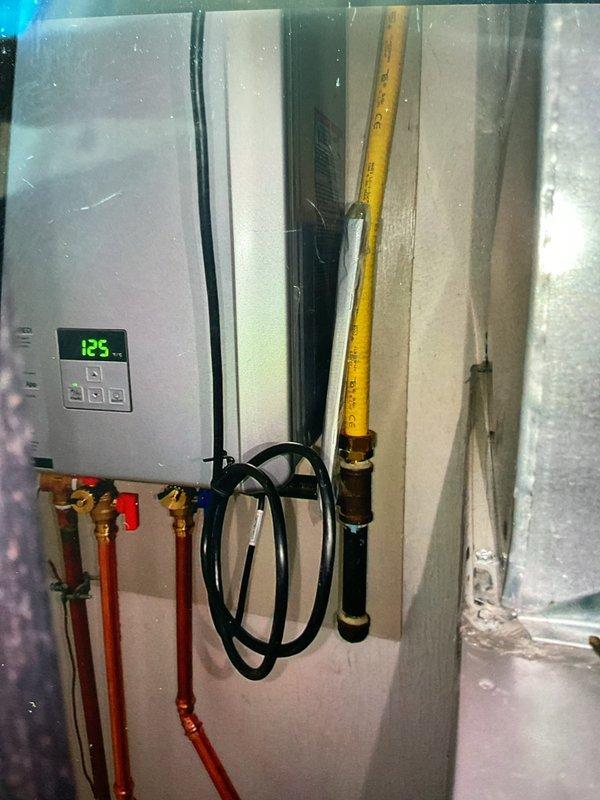 Replaced existing Rinnai RL75 tankless water heater with new Rinnai 180 unit in utility area. Installation included mounting unit on concrete board backing, connecting copper water inlet and outlet lines with shut-off valves, installing yellow CSST gas line with safety shut-off valve, and routing white PVC venting through wall. Unit tested and operational with digital display functioning properly, all connections verified leak-free, and system staged with navigation kit per manufacturer specifications.