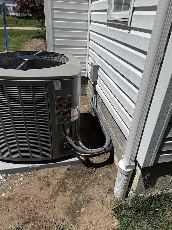 Completed full HVAC system installation including a 97% high-efficiency furnace, air conditioning condenser unit, and humidifier. The furnace was installed in the basement utility area on a wooden platform with proper ductwork connections and black flexible ducting integrated into the existing overhead duct system. The outdoor AC condenser unit was positioned on the building's exterior with refrigerant lines properly insulated and routed along the foundation and up the exterior wall. A PVC condensate drain line was installed and mounted vertically on the building exterior. All components were installed to manufacturer specifications with appropriate clearances, electrical connections completed, and system tested for proper operation.