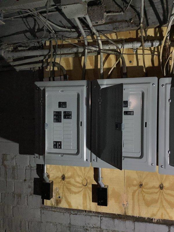 Conducted site assessment of existing electrical service in basement utility area. Evaluated two white electrical panel boxes with exposed circuit breakers mounted on plywood backing against concrete block foundation. Inspected condition of panels, breakers, and associated wiring including metallic and PVC conduits running through floor joists. Assessed black disconnect boxes and junction boxes mounted below main panels. 

Evaluated unfinished basement space with exposed brick walls and determined requirements for establishing proper electrical service to the dwelling. Documented existing infrastructure including overhead piping, ductwork, and cable runs. Identified need for new service entrance conductors and potential panel replacement due to age and configuration of current installation. Photographed existing conditions including panel interiors, conduit routing, and structural elements for quote preparation. Coordinated assessment with plumbing contractor also working on property t
