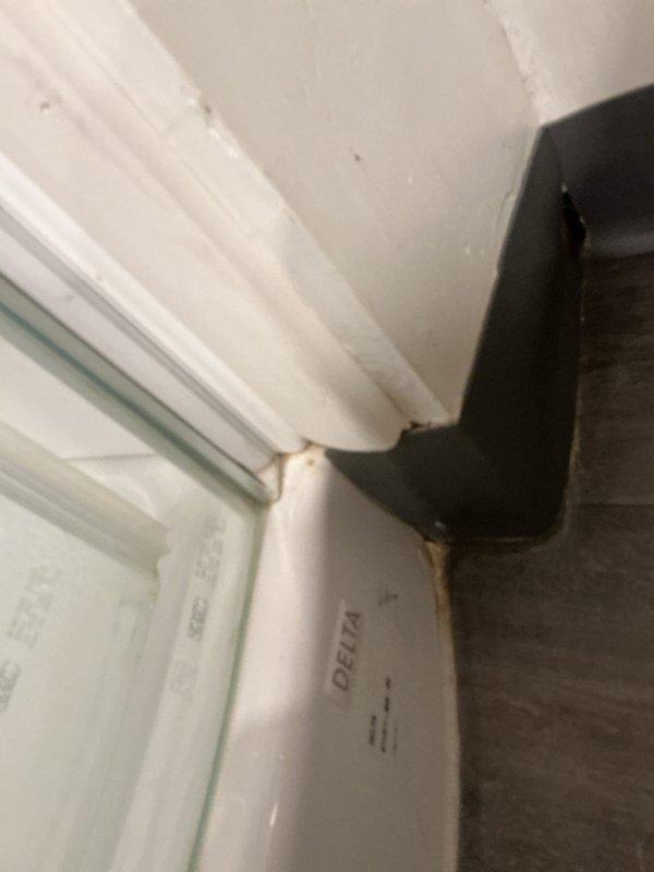 Responded to service call for reported shower leak. Upon inspection, identified moisture infiltration at shower enclosure corner joint with visible water staining and discoloration along wall-to-floor seam. Examined Delta shower fixture installation and surrounding plumbing connections. Documented deteriorated caulking and seal failure at corner junction where vertical supply line meets the enclosure, allowing water to escape during shower use. Assessed exposed piping for additional leak sources and confirmed primary issue at compromised sealant joint requiring re-caulking and potential trim adjustment to prevent future water damage.