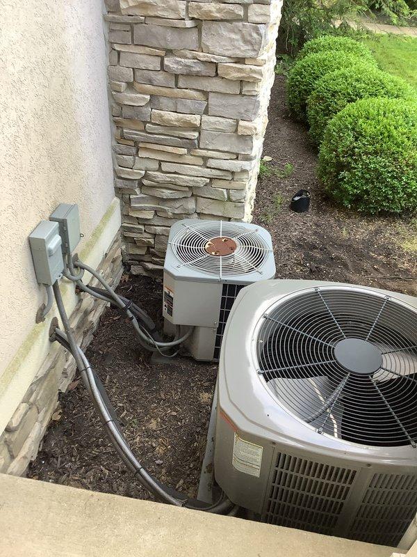 Completed full HVAC system installation including 80% efficiency furnace, air conditioning system with dual outdoor condenser units, whole-home humidifier, and tankless water heater. Installed two white condensing units on exterior mulch bed with proper clearance for airflow and maintenance access. Ran electrical conduit and copper refrigerant lines from wall-mounted disconnect boxes to equipment following building exterior. Positioned indoor air handler in basement utility area with new sheet metal ductwork. Installed condensate management system including green condensate pump, white PVC drain lines with proper pitch and support, and black flexible discharge tubing. All components tested and verified operational upon completion. System installation meets manufacturer specifications and local building codes.