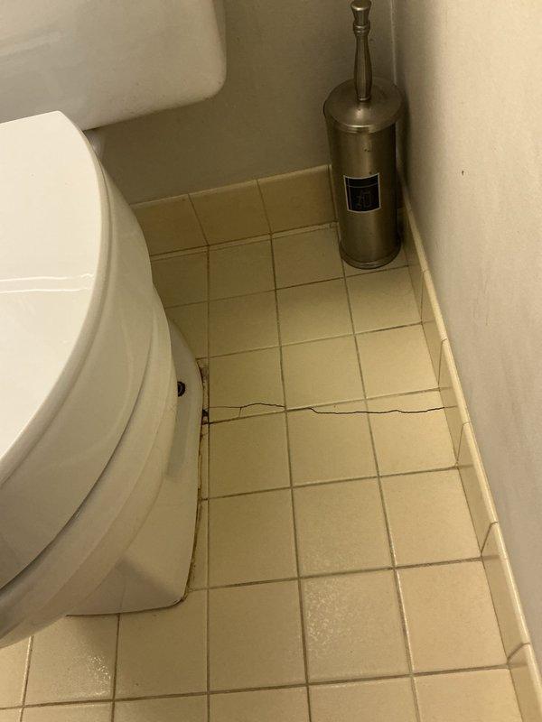 Responded to a plumbing emergency involving water leaking from the base of a toilet that was seeping through the floor and causing significant water damage to the ceiling below. Upon inspection, identified a failed wax ring seal at the toilet base, removed and reset the toilet with a new wax ring and closet bolts, and verified proper seal and stability. Documented extensive water damage to the bathroom floor tiles (visible cracking) and ceiling damage in the room below, including water staining, structural deterioration, and compromised drywall requiring future remediation by appropriate trades.