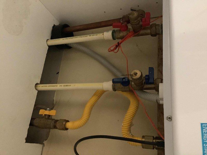 Responded to service call for tankless water heater with no hot water production affecting entire home. Upon arrival, accessed utility closet and inspected white cylindrical tankless unit and associated plumbing connections. Evaluated gas supply line with yellow corrugated flexible connector, brass gas valve with control handle, water supply lines including PVC piping, shut-off valves (red and blue handled ball valves), and electrical connections. Documented existing installation configuration showing proper gas line routing, multiple shut-off points for isolation capability, and water inlet/outlet connections via large diameter PVC pipes. Photographed accessible plumbing assembly within wall cavity including all supply lines, valves, and safety components for maintenance records. Verified gas supply availability and proper valve positioning. Assessed unit placement in confined space with adequate ventilation access. Noted ceiling condition in installation area. System evaluation compl