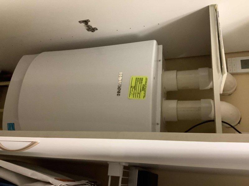 Responded to service call for tankless water heater with no hot water production affecting entire home. Upon arrival, accessed utility closet and inspected white cylindrical tankless unit and associated plumbing connections. Evaluated gas supply line with yellow corrugated flexible connector, brass gas valve with control handle, water supply lines including PVC piping, shut-off valves (red and blue handled ball valves), and electrical connections. Documented existing installation configuration showing proper gas line routing, multiple shut-off points for isolation capability, and water inlet/outlet connections via large diameter PVC pipes. Photographed accessible plumbing assembly within wall cavity including all supply lines, valves, and safety components for maintenance records. Verified gas supply availability and proper valve positioning. Assessed unit placement in confined space with adequate ventilation access. Noted ceiling condition in installation area. System evaluation compl