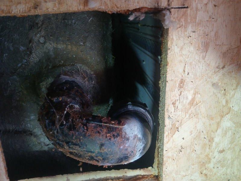 Performed diagnostic inspection on bathtub drainage system in manufactured home. Accessed plumbing beneath unit through crawl space entry point at foundation. Inspection revealed severely corroded P-trap assembly with extensive rust deterioration throughout the curved pipe section, indicating prolonged moisture exposure and compromised structural integrity. The metal trap exhibited heavy oxidation with reddish-brown surface degradation requiring complete replacement. Documented existing conditions with photographs showing corroded trap through access panel and exterior crawl space work area. Prepared ground area with protective tarp for undercarriage access. Provided diagnostic findings and recommended full bathtub drain assembly replacement, which will require working beneath the doublewide trailer structure to properly install new components.