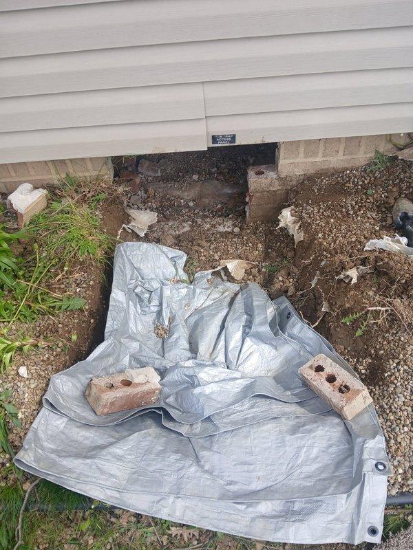 Performed diagnostic inspection on bathtub drainage system in manufactured home. Accessed plumbing beneath unit through crawl space entry point at foundation. Inspection revealed severely corroded P-trap assembly with extensive rust deterioration throughout the curved pipe section, indicating prolonged moisture exposure and compromised structural integrity. The metal trap exhibited heavy oxidation with reddish-brown surface degradation requiring complete replacement. Documented existing conditions with photographs showing corroded trap through access panel and exterior crawl space work area. Prepared ground area with protective tarp for undercarriage access. Provided diagnostic findings and recommended full bathtub drain assembly replacement, which will require working beneath the doublewide trailer structure to properly install new components.