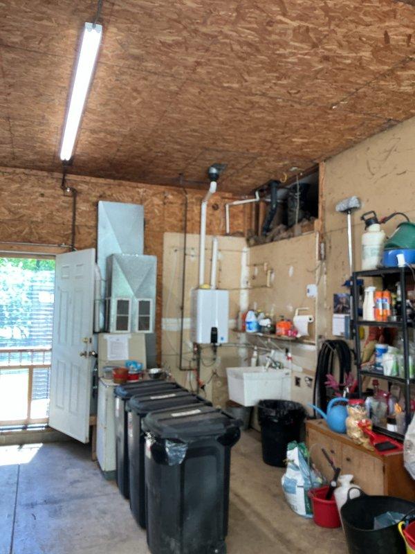 Responded to no hot water complaint affecting entire home. Upon arrival, diagnosed wall-mounted tankless water heater unit in garage utility area with failure to ignite. Inspected unit and associated PVC venting system, electrical connections, and gas supply lines. Restored hot water functionality to residence. Documented installation with photos showing tankless unit mounted on OSB wall with proper venting configuration and plumbing connections intact.