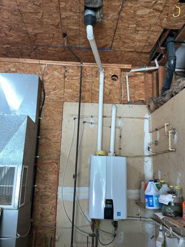 Responded to no hot water complaint affecting entire home. Upon arrival, diagnosed wall-mounted tankless water heater unit in garage utility area with failure to ignite. Inspected unit and associated PVC venting system, electrical connections, and gas supply lines. Restored hot water functionality to residence. Documented installation with photos showing tankless unit mounted on OSB wall with proper venting configuration and plumbing connections intact.