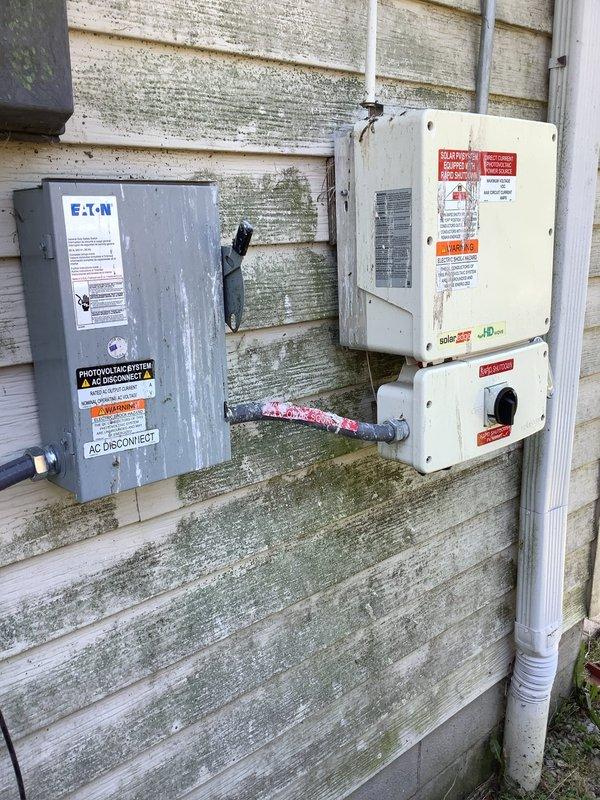 Responded to service call for exterior main breaker repeatedly tripping, with customer reporting issue worsening during hot weather and breaker running hot to touch after shutting off all 220V appliances. Upon arrival, inspected exterior electrical service panel and photovoltaic system AC disconnect mounted on building exterior. Found main breaker exhibiting signs of thermal stress and heat-related failure. Conducted thermal assessment of breaker and connections, identifying excessive heat buildup in main breaker assembly during high ambient temperature conditions. Documented existing electrical service configuration including meter base, main disconnect, and solar system integration points. Photographed weathered exterior panel installation showing EATON service equipment and associated solar disconnect enclosure with conduit connections. Issue determined to be heat-related breaker degradation causing nuisance tripping under load during elevated outdoor temperatures. Recommended break