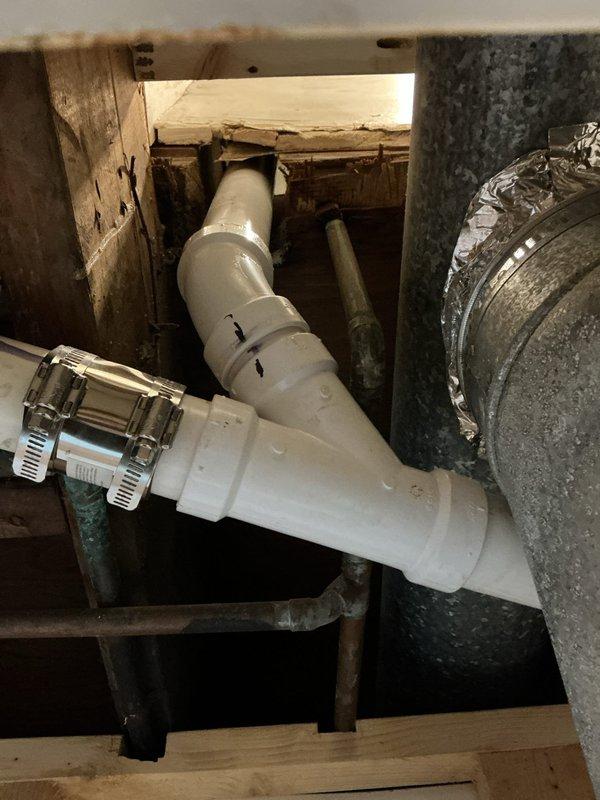 Replaced deteriorated cast iron drain lines with new PVC piping from 4-inch fernco connection to back-to-back bathroom group configuration. Removed existing cast iron drainage system and installed white PVC drain pipes with proper fittings, elbows, and couplings through wooden floor framing. Secured all piping with appropriate clamps and supports, ensuring proper pitch and alignment for optimal drainage flow. Two-person crew completed full-day installation including rough-in plumbing work through subfloor and structural framework.
