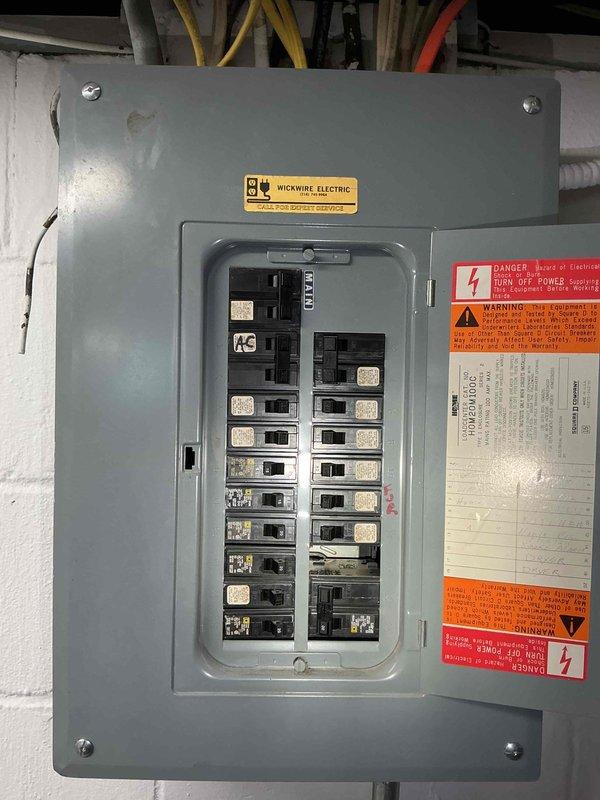 Installed sub panel for exterior barn structure. Mounted gray electrical panel enclosure on white block wall with proper clearances and accessibility. Wired panel with appropriate feeder conductors and established circuit breaker configuration for barn electrical distribution. Panel labeled with contractor identification and all required safety warnings, danger labels, and code compliance documentation affixed to interior door. Verified proper grounding, torqued all connections to manufacturer specifications, and ensured panel meets current electrical code requirements for outbuilding installations.