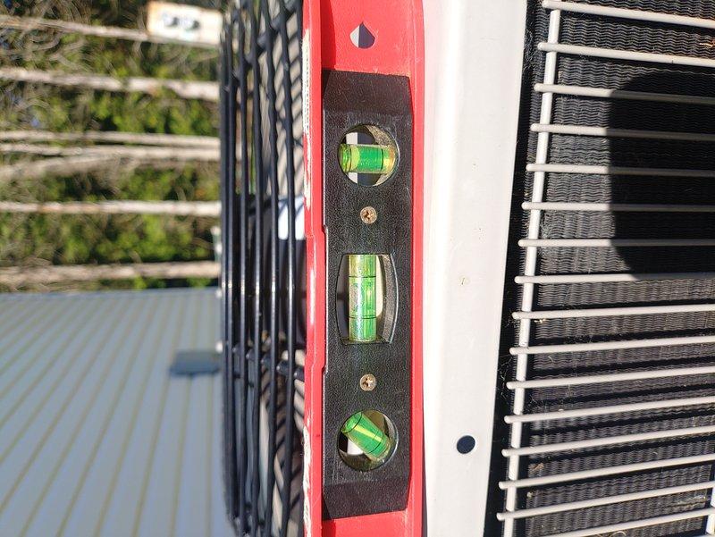 Responded to service call for unlevel 9-year-old air conditioning unit that had settled and was sinking on one side. Upon inspection, confirmed unit was significantly out of level using spirit level, with visible gap beneath the condenser pad where soil had compacted and eroded over time. Leveled and stabilized the outdoor condensing unit to ensure proper refrigerant oil return, prevent compressor damage, and restore optimal system operation.