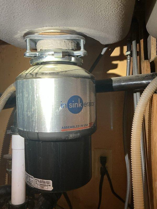 Responded to service call for leaking garbage disposal unit beneath kitchen sink. Upon inspection, identified leak originating from InSinkErator disposal unit's mounting assembly and drain connections. Tightened mounting flange and securing mechanisms at sink drain opening, then inspected and resealed discharge tube connections where black rubber hoses attach to disposal housing. Verified all plumbing connections were secure and tested unit operation to confirm leak was resolved. Unit returned to proper working condition with no further water discharge detected.