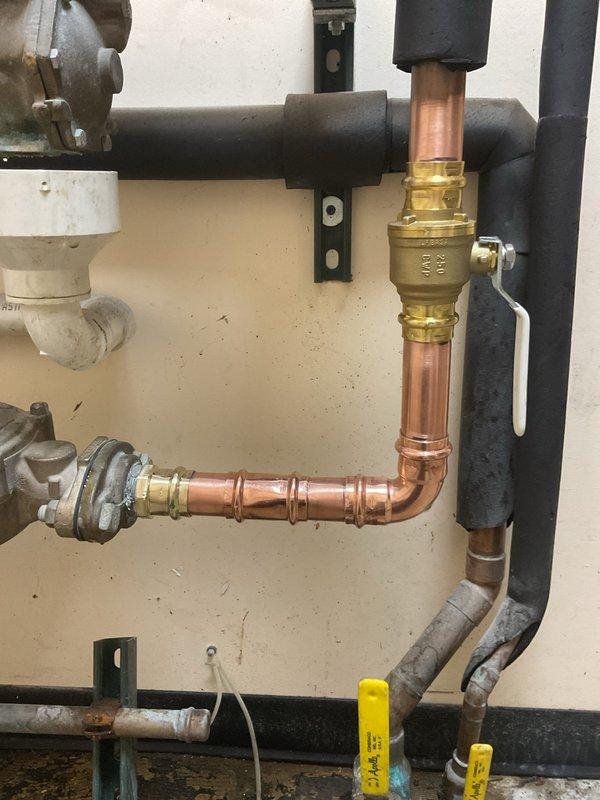 Responded to a leak at a 1 1/2 x 1 x 1 1/2 copper tee fitting located on the outlet side of the water meter. Rebuilt the configuration from the meter flange, eliminating the problematic 1-inch pipe section, installed a new brass ball valve on the vertical copper pipe run, and securely reconnected all components to the meter flange. The repair successfully resolved the leak and restored proper water flow to the system.