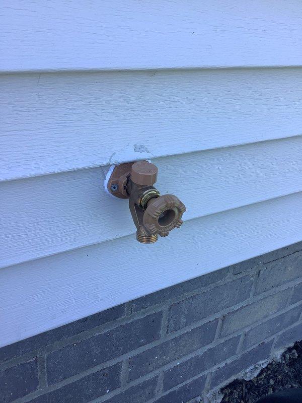 Responded to service call for leaking outdoor spigot. Upon inspection, identified active leak at hose bib mounted on exterior wall with white vinyl siding. Accessed plumbing from interior crawl space and found the spigot was plumbed with PEX tubing. Installed new shut-off valve with red handle and integrated white pressure regulator into the blue PEX line to provide proper isolation and flow control. Secured all connections with appropriate clamps and fittings to ensure leak-free operation. Tested system for proper function and verified no additional leaks present. Outdoor spigot now operating correctly with full shut-off capability.