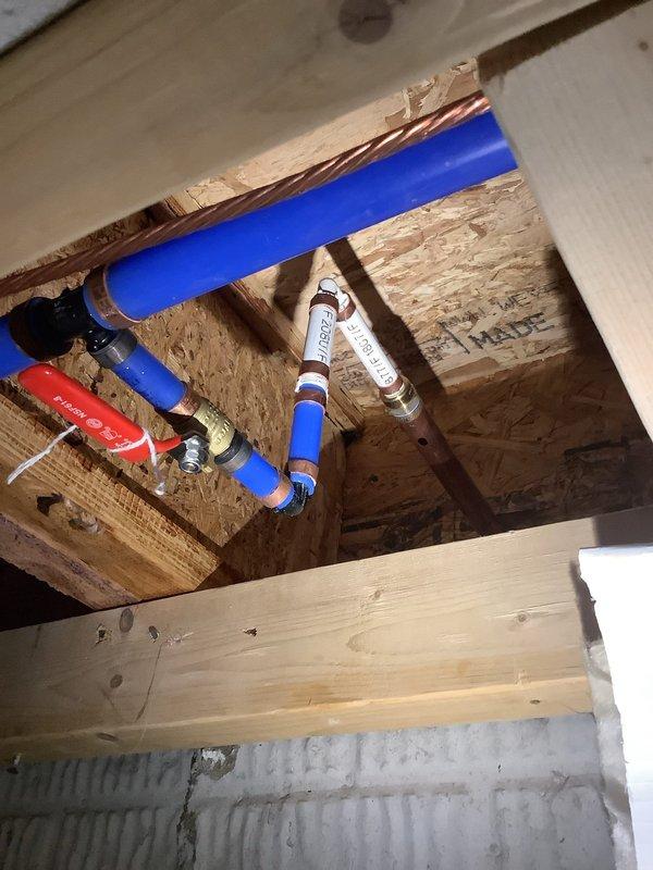 Responded to service call for leaking outdoor spigot. Upon inspection, identified active leak at hose bib mounted on exterior wall with white vinyl siding. Accessed plumbing from interior crawl space and found the spigot was plumbed with PEX tubing. Installed new shut-off valve with red handle and integrated white pressure regulator into the blue PEX line to provide proper isolation and flow control. Secured all connections with appropriate clamps and fittings to ensure leak-free operation. Tested system for proper function and verified no additional leaks present. Outdoor spigot now operating correctly with full shut-off capability.
