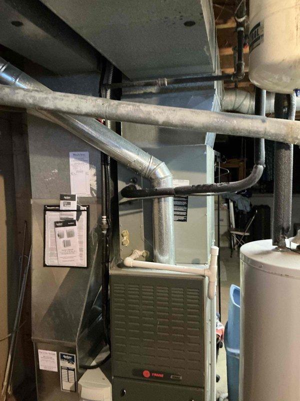 Conducted on-site HVAC system evaluation for equipment replacement estimate in residential basement mechanical room. Assessed existing 12-year-old Trane furnace, air handler unit, and associated ductwork configuration. Documented current system layout including metallic supply ductwork, flexible return ducts, and equipment placement relative to water heater and utility infrastructure. Applied veteran discount to quoted replacement pricing and captured photographic documentation of existing equipment conditions for proposal reference.